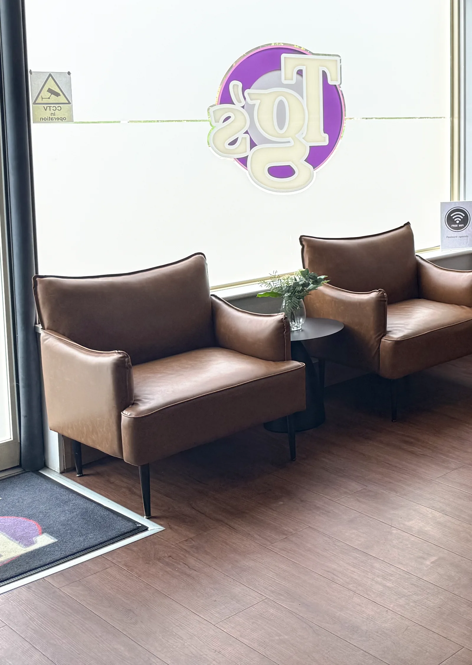 Two tan leather armchairs and a side table in the Higham Ferrers waiting area, below the TG's roundel on the window