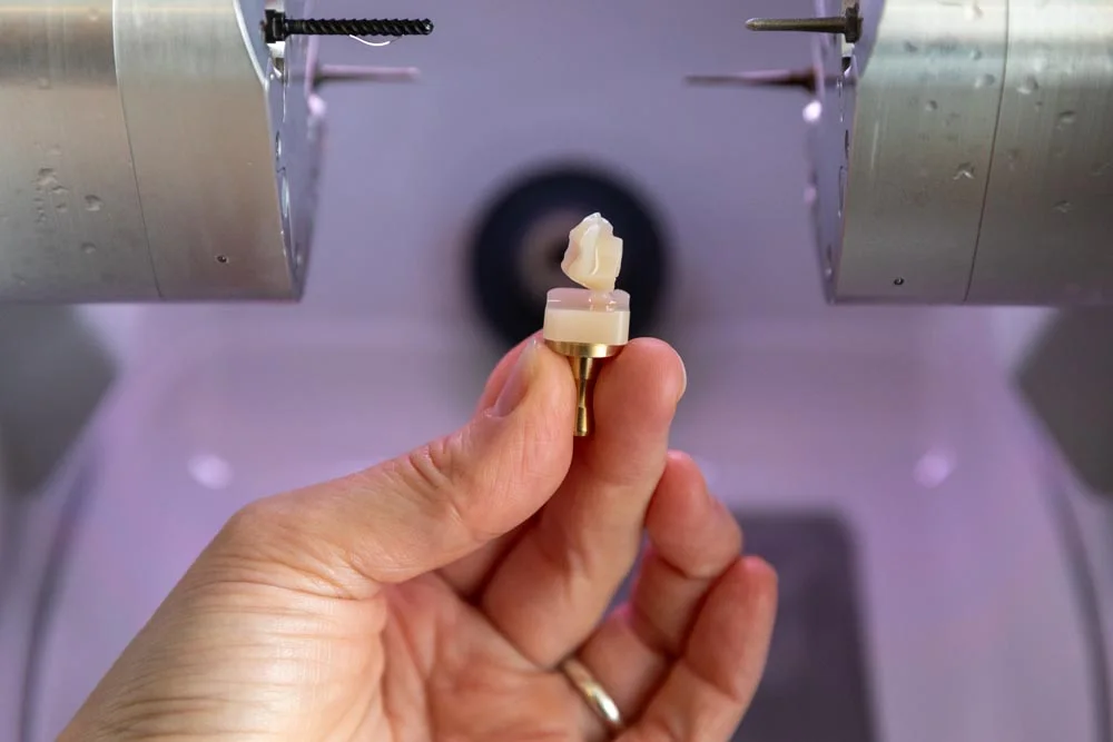 Close-up of a milled ceramic crown held beside the CEREC milling unit