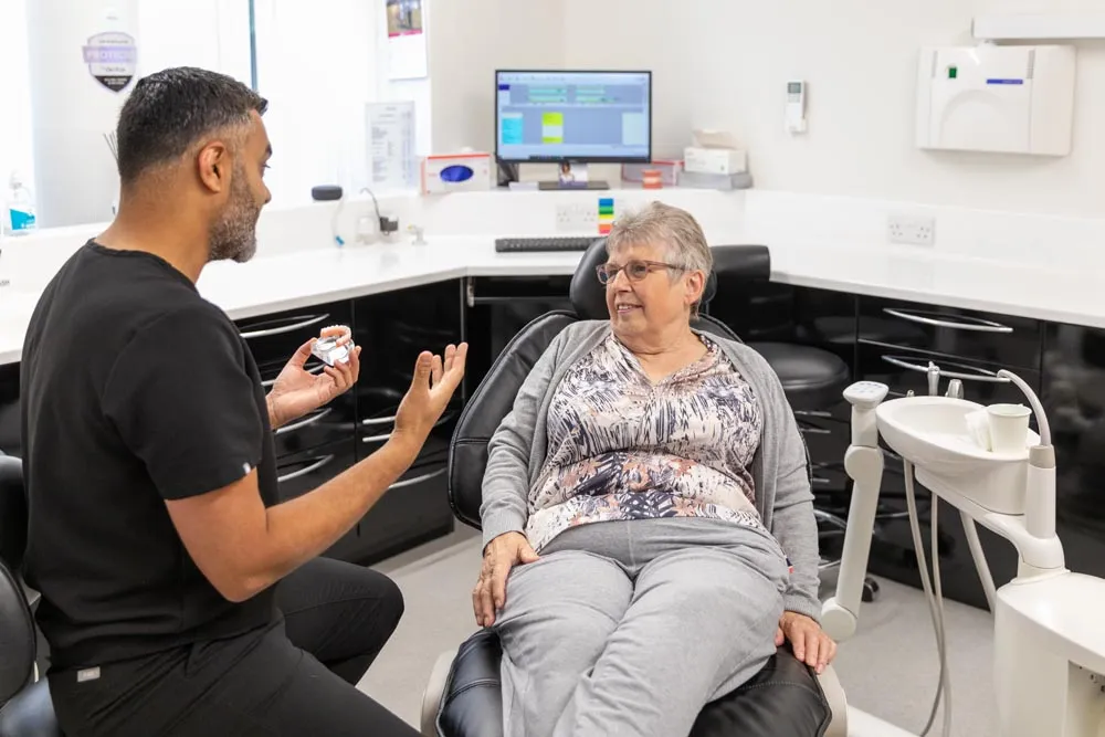 Clinician talking through a dental model with an older patient seated in the treatment chair